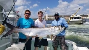 The crew and angler holding up a giant tarpon they just caught in the Ft Lauderdale Intracoastal waterway.