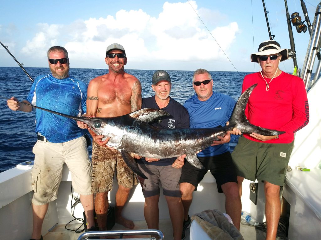 Group of guys on a swordfishing charter, holding a 100+ pound swordfish they just caught.
